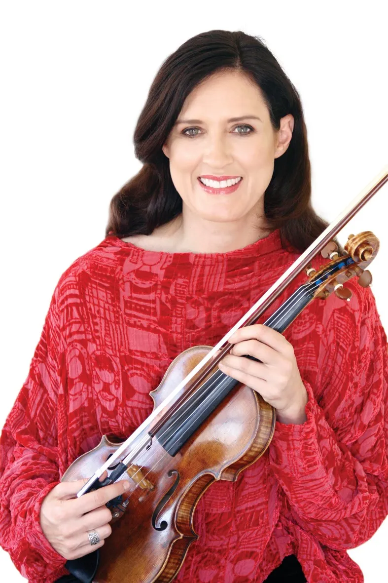 Smiling Zanta Hofmeyr in a textured red blouse, cradling her violin and bow against her chest in front of a white background